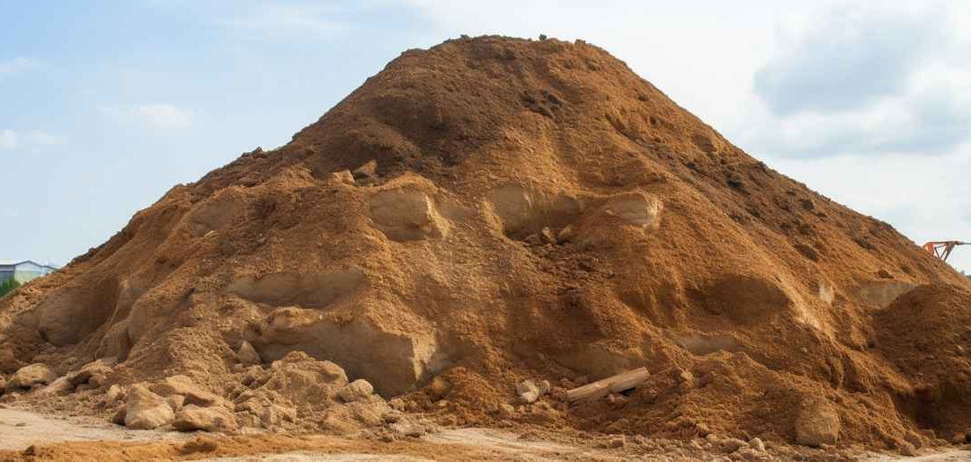 Bild zeigt einen Haufen Erdaushub auf einer Baustelle. Die erdigen Materialien variieren in Farbe und Textur, was auf eine Mischung aus Boden, Sand und Kies hinweist.